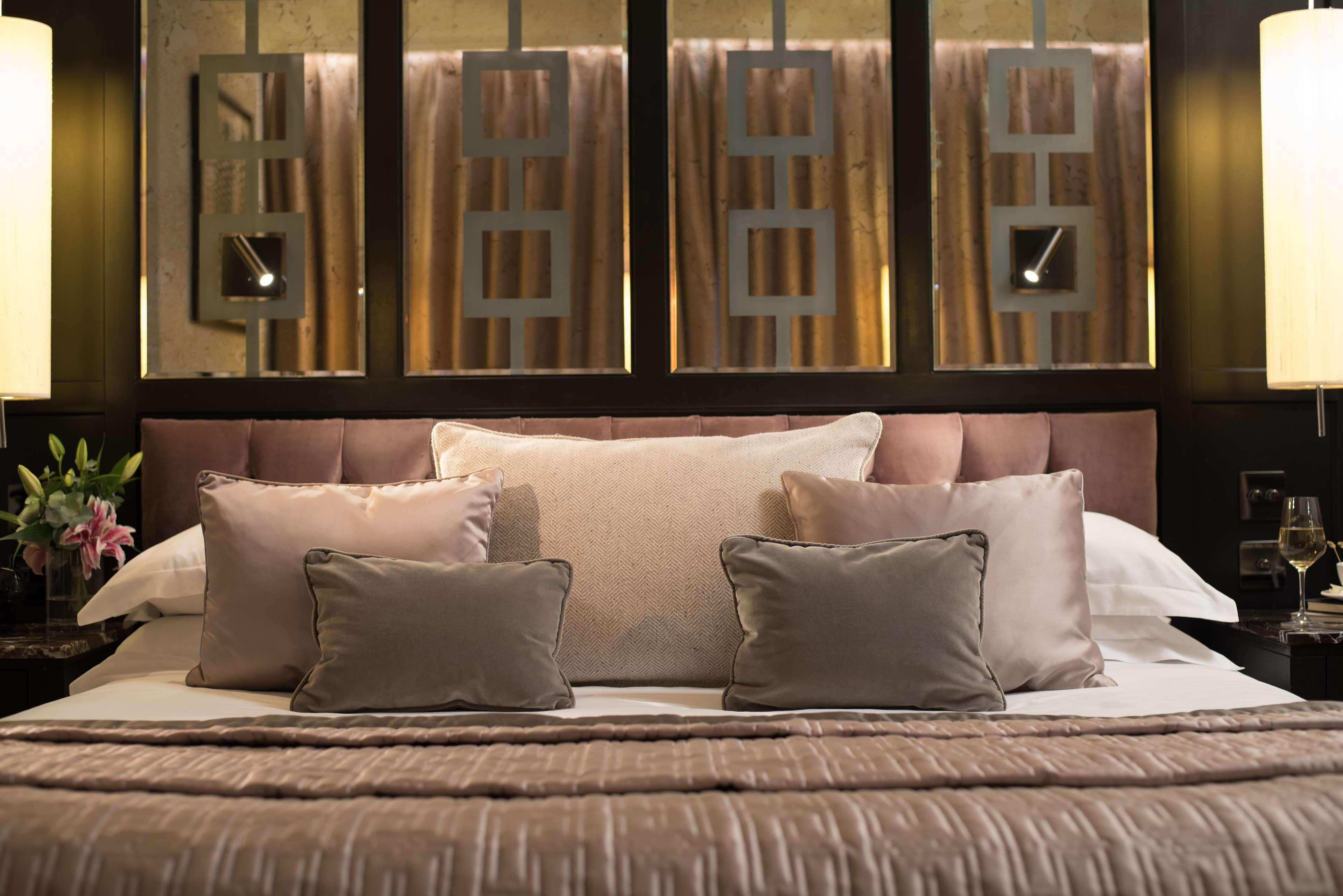 The Fitzwilliam Hotel Belfast Luaran gambar The photo shows a beautifully designed bed in a stylish bedroom. The bed is adorned with a soft, plush headboard and layered with various decorative pillows in shades of beige and gray. The bedding appears luxurious, with a textured blanket. Behind t