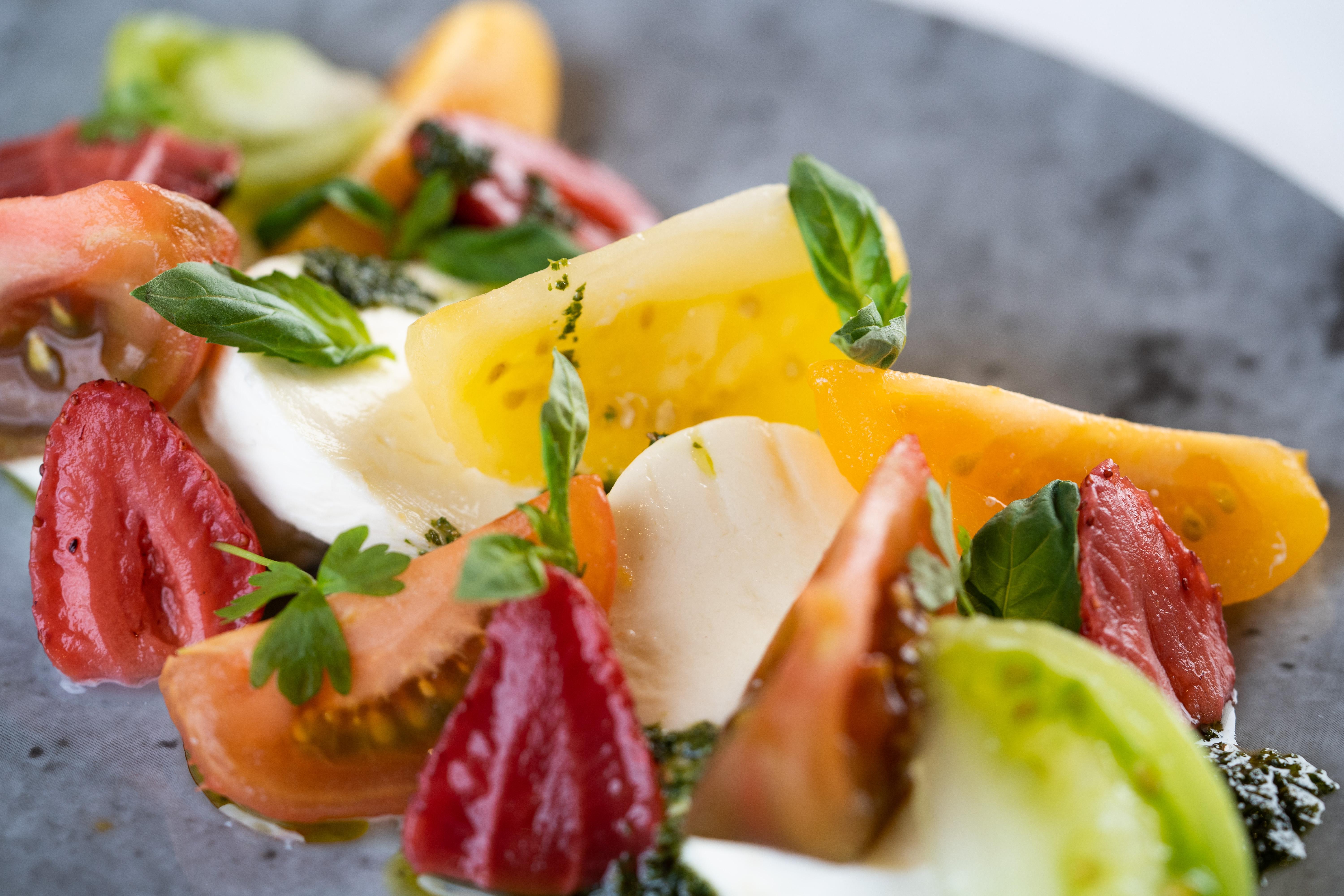 The Fitzwilliam Hotel Belfast Luaran gambar The photo shows a vibrant salad featuring slices of various tomatoes, including red, yellow, and green varieties. The tomatoes are paired with fresh mozzarella cheese and garnished with basil leaves. The dish is presented on a round, dark plate, high